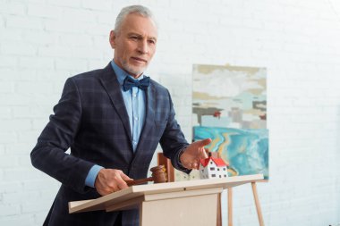 Müzayedeci ev modelini işaret ediyor ve açık arttırma sırasında tokmağı tutuyor.
