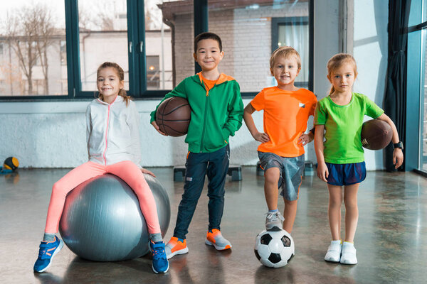 Вид спереди ребенка, сидящего на фитнес-мяче рядом с детьми с мячами в тренажерном зале

