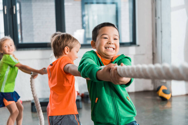 Selective focus of multicultural kids playing tug of war in gym