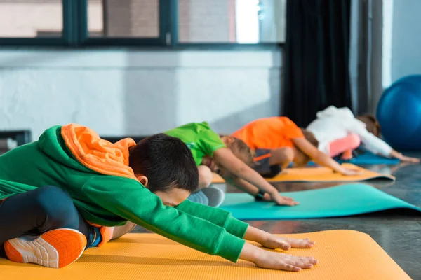 Foco Seletivo Crianças Multiétnicas Com Pernas Cruzadas Esticadas Tapetes Fitness — Fotografia de Stock
