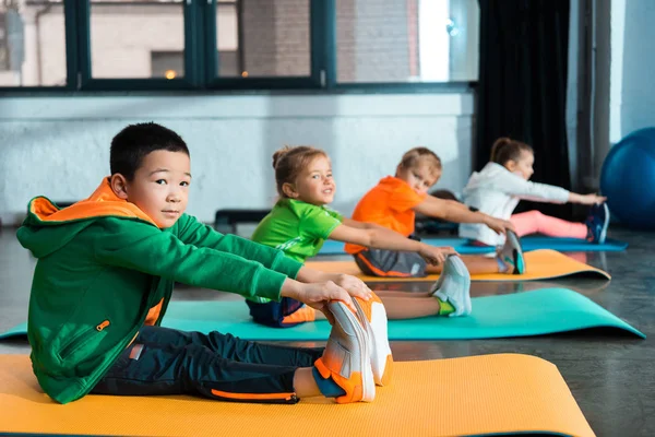 Επιλεκτική Εστίαση Πολυεθνικών Παιδιών Που Εκτείνονται Στρώματα Γυμναστικής Στο Αθλητικό — Φωτογραφία Αρχείου