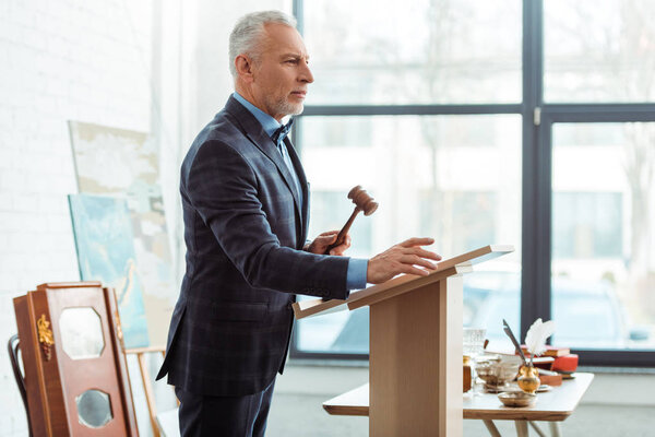 вид сбоку на аукциониста, держащего деревянную жезл и отводящего взгляд во время аукциона
