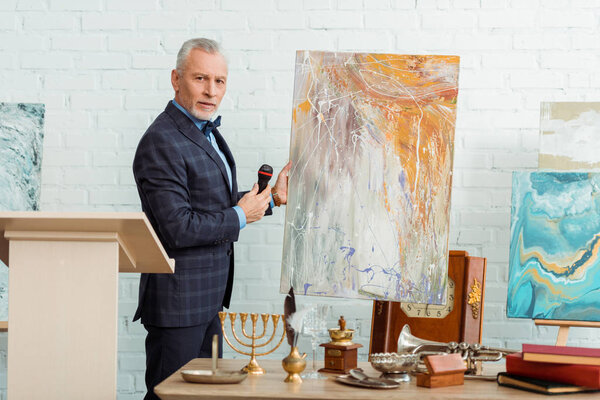 auctioneer talking with microphone and standing near picture during auction