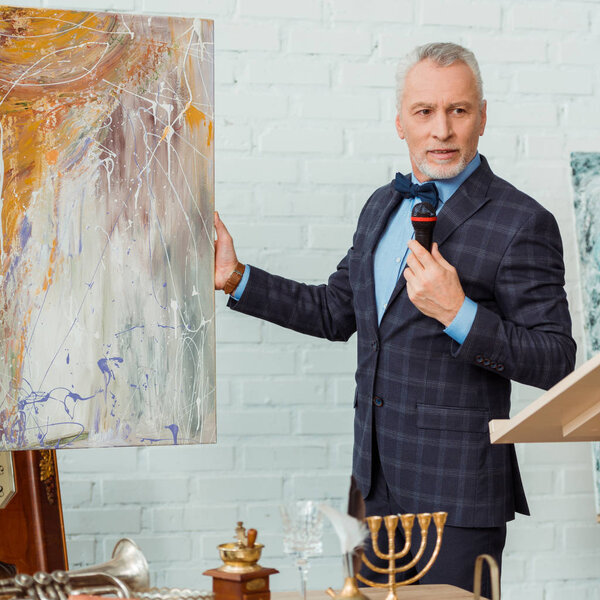 аукционист разговаривает с микрофоном и держит фотографию во время аукциона
