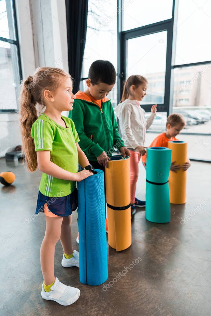 Selective focus of multicultural children standing with fitness mats in gym