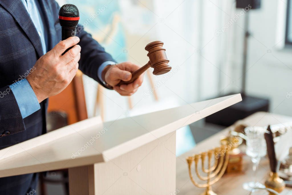 cropped view of auctioneer in suit talking with microphone and holding gavel during auction