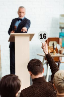 back view of buyer showing auction paddle with number sixteen to auctioneer during auction clipart