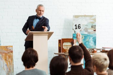 selective focus of auctioneer holding gavel and pointing with finger at buyer during auction clipart