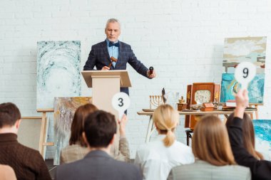Elinde tokmak ve mikrofon tutan ve açık arttırma sırasında alıcılara bakan açık arttırmacı seçici odağı
