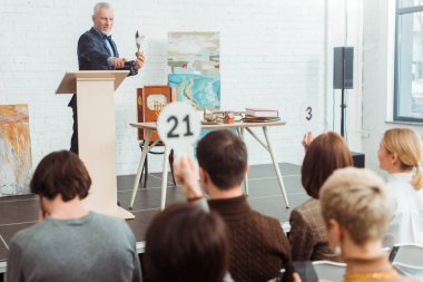 selective focus of smiling auctioneer holding feather pen and pointing with finger at buyer during auction clipart