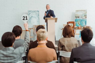 selective focus of auctioneer holding talking with microphone and looking at buyer during auction clipart