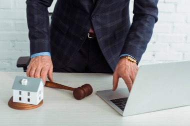 cropped view of auctioneer holding gavel and using laptop  clipart