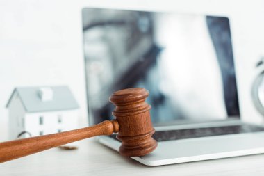 selective focus of wooden gavel near laptop and model of house  clipart