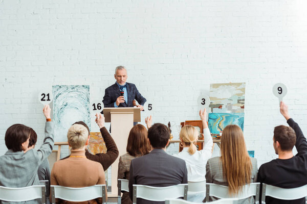 auctioneer talking with microphone and looking at buyers with auction paddles during auction