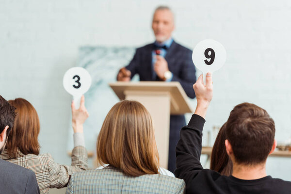 back view of buyers showing auction paddles with numbers nine and three to auctioneer during auction