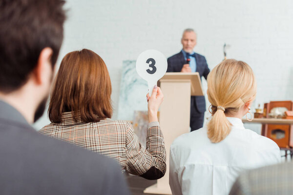 back view of buyer showing auction paddle with number three to auctioneer during auction