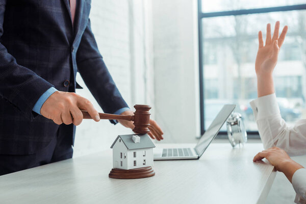 cropped view of auctioneer hitting with gavel model oh house and woman raising hand 