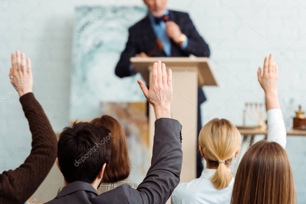 back view of buyers raising hands to auctioneer during auction