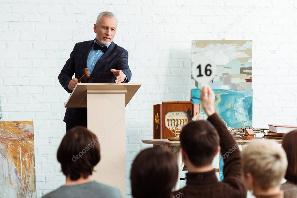 selective focus of auctioneer holding gavel and pointing with finger at buyer during auction