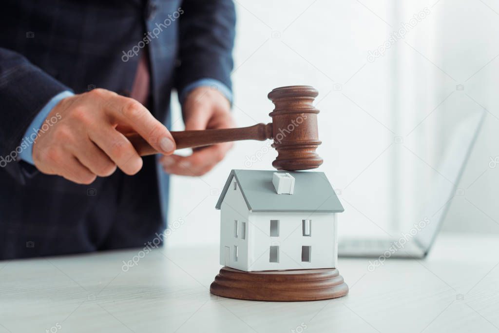 cropped view of auctioneer hitting model of house with gavel 