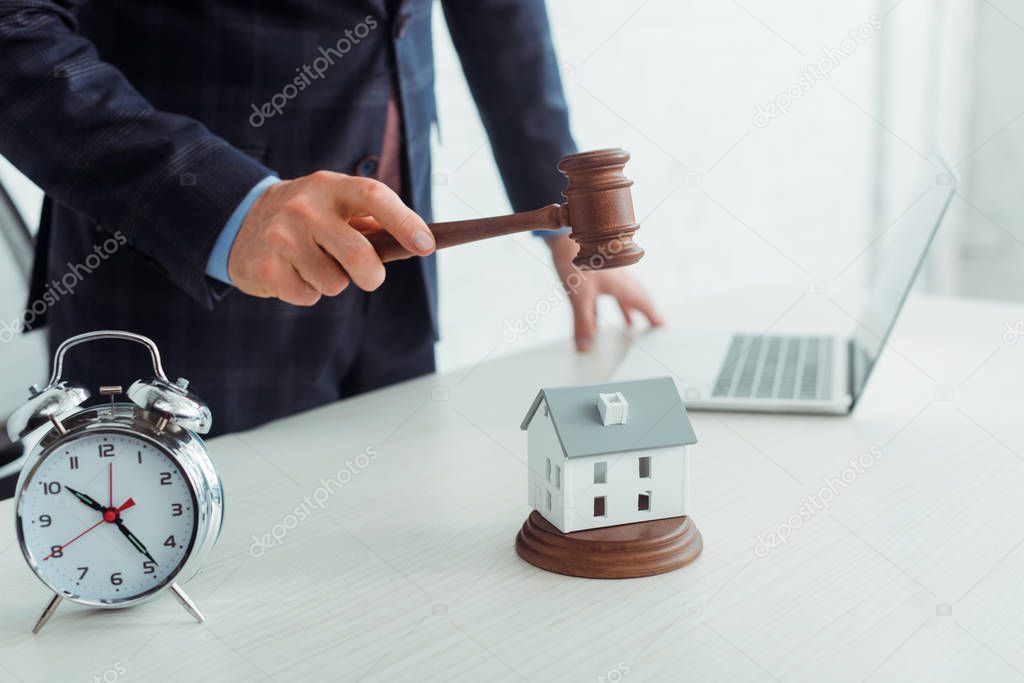 cropped view of auctioneer hitting model of house with gavel 