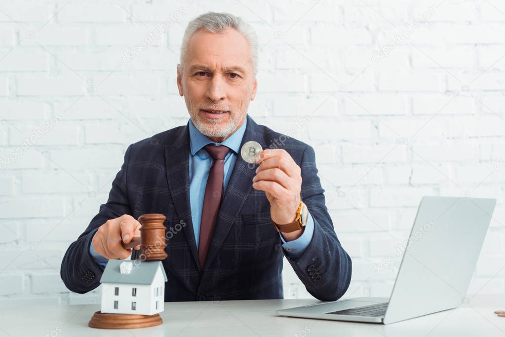 handsome auctioneer hitting model of house with gavel and holding coins 