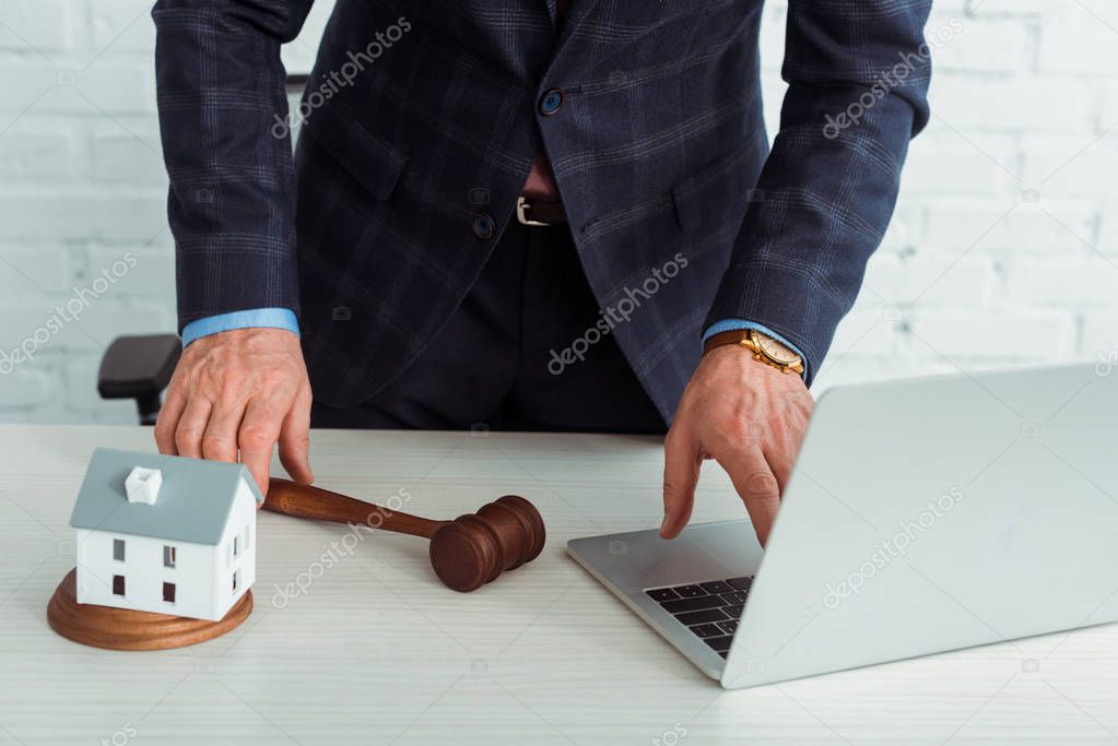 cropped view of auctioneer holding gavel and using laptop 