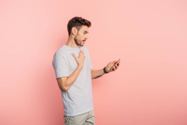 Pembe arka planda akıllı telefonu tutarken göğsüne dokunan genç adam şaşırdı.