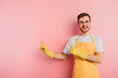 Önlüklü mutlu genç adam ve pembe arka planda parmakları olan lastik eldivenler.