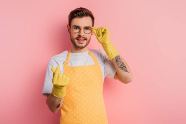 Önlüklü ve lastik eldivenli gülümseyen genç adam pembe arka planda ne kadar para olduğunu gösteriyor.