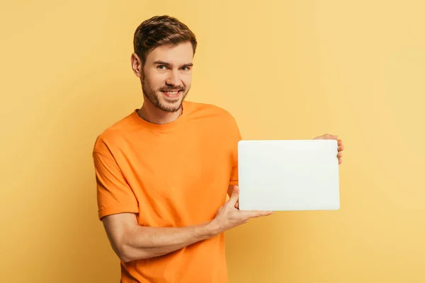 Smiling Young Man Showing Closed Laptop Looking Camera Yellow Background — Stock Photo, Image