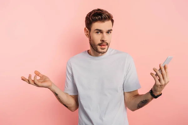Σύγχυση Νεαρός Άνδρας Δείχνει Shrug Χειρονομία Ενώ Κρατώντας Smartphone Ροζ — Φωτογραφία Αρχείου
