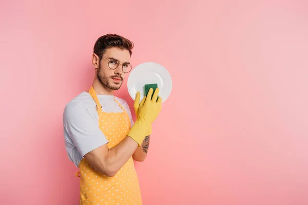 Serious Young Man Apron Rubber Gloves Cleaning Plate Sponge Pink — Stock Photo, Image
