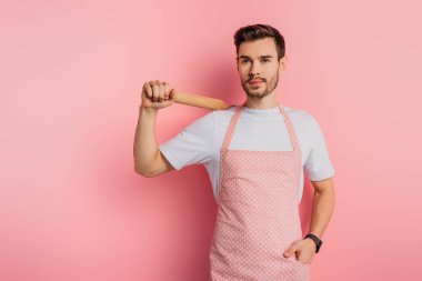 Pembe arka planda el ele dururken önlüklü neşeli genç adam merdaneyi tutuyor.