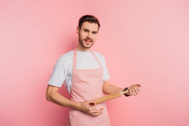 Önlüklü genç adam pembe arka planda raptiyeyle gitar çalıyormuş gibi yapıyor.