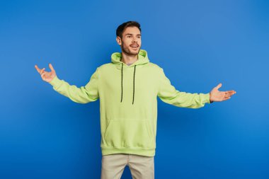 Mutlu yakışıklı adam mavi arka planda kolları açık dururken başka tarafa bakıyor.