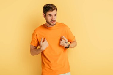 Kızgın genç adam, sarı arka plana bakarken parmaklarıyla işaret ediyor.