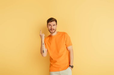 tricky young man showing idea gesture on yellow background clipart