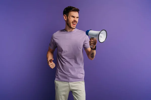 Jovem Irritado Gritando Megafone Enquanto Olha Para Fundo Roxo — Fotografia de Stock