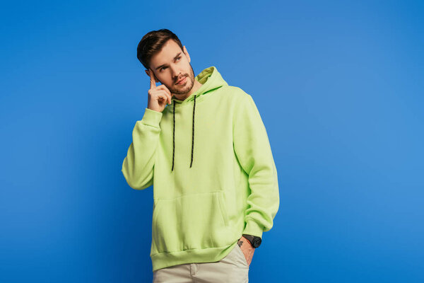 вдумчивый молодой человек касается головы и смотрит в сторону на голубом фоне
