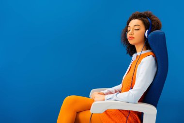 Eski moda elbiseli Afrikalı Amerikalı müzik dinliyor ve mavi koltukta tek başına uyuyor. 