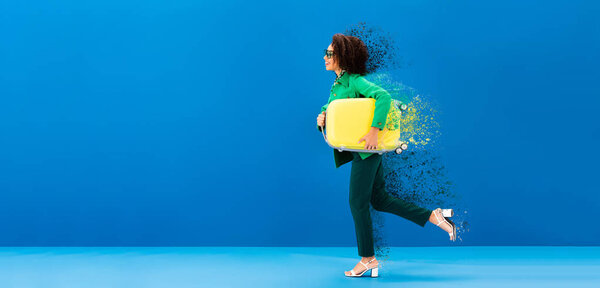 panoramic shot of smiling african american woman running with travel bag on blue background 