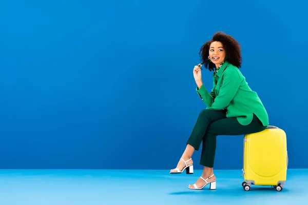 Mujer Afroamericana Sonriente Sosteniendo Gafas Sol Sentada Una Bolsa Viaje — Foto de Stock