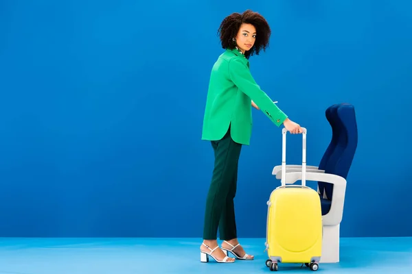 拿着旅行袋站在蓝色背景座位旁边的非洲裔美国女人 — 图库照片