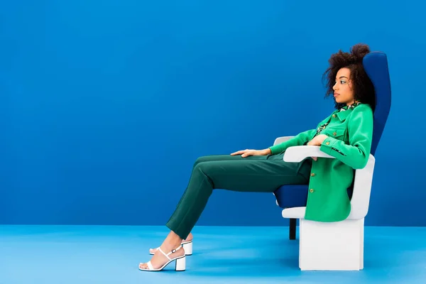 Vista Lateral Elegante Mujer Afroamericana Sentada Asiento Sobre Fondo Azul —  Fotos de Stock