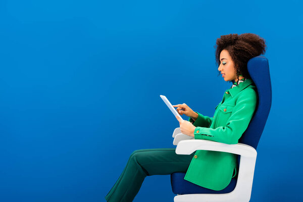 side view of african american woman using digital tablet isolated on blue 