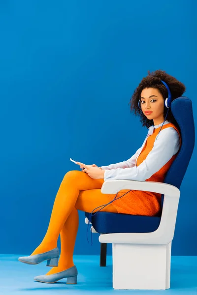 Africký Američan Retro Šaty Sedí Sedadle Poslech Hudby Modrém Pozadí — Stock fotografie