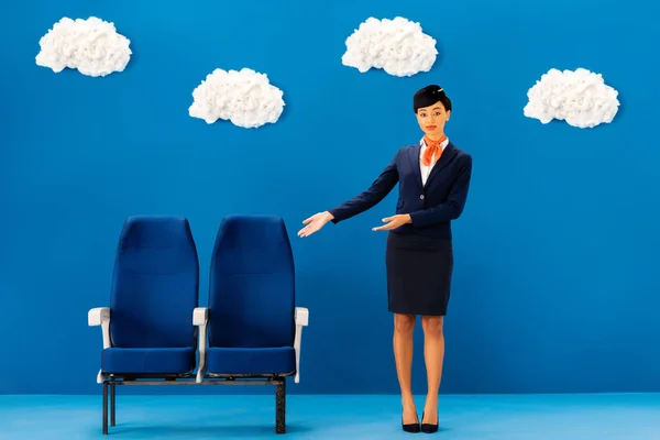 Афроамериканська Стюардеса Вказує Руками Сидіння Синьому Фоні Хмарами — стокове фото