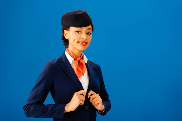 smiling african american flight attendant looking at camera isolated on blue