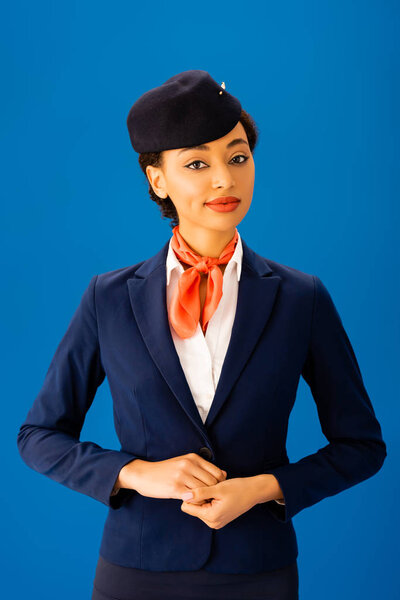 smiling african american flight attendant  looking at camera isolated on blue